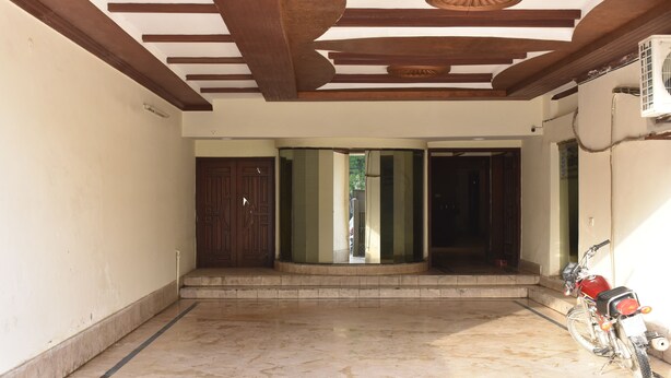 A spacious indoor area with a tiled floor, a motorcycle parked near a wall, and a door leading to another room. - Bright Hotel (Lahore)