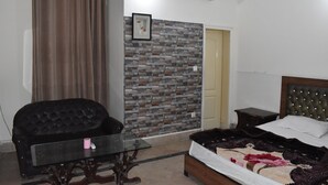 A bedroom with a brick-patterned wall, a bed with a decorative headboard, a small table, and a chair. - Bright Hotel (Lahore)