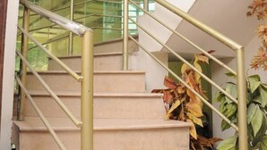 A staircase with beige steps and gold handrails, leading to a landing with a glass railing. - Bright Hotel (Lahore)