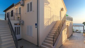 A two-story building with a staircase, a balcony, and a view of the sea.