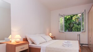 A bedroom with a wooden bed, two bedside lamps, a window with a view of greenery, and a radiator.