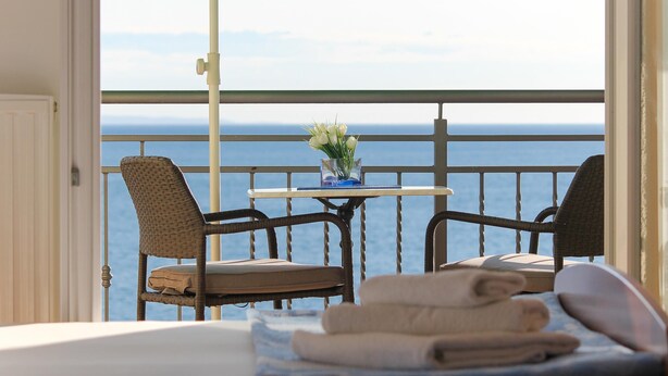 A balcony with wicker chairs, a small table with a vase of flowers, and a view of the sea.