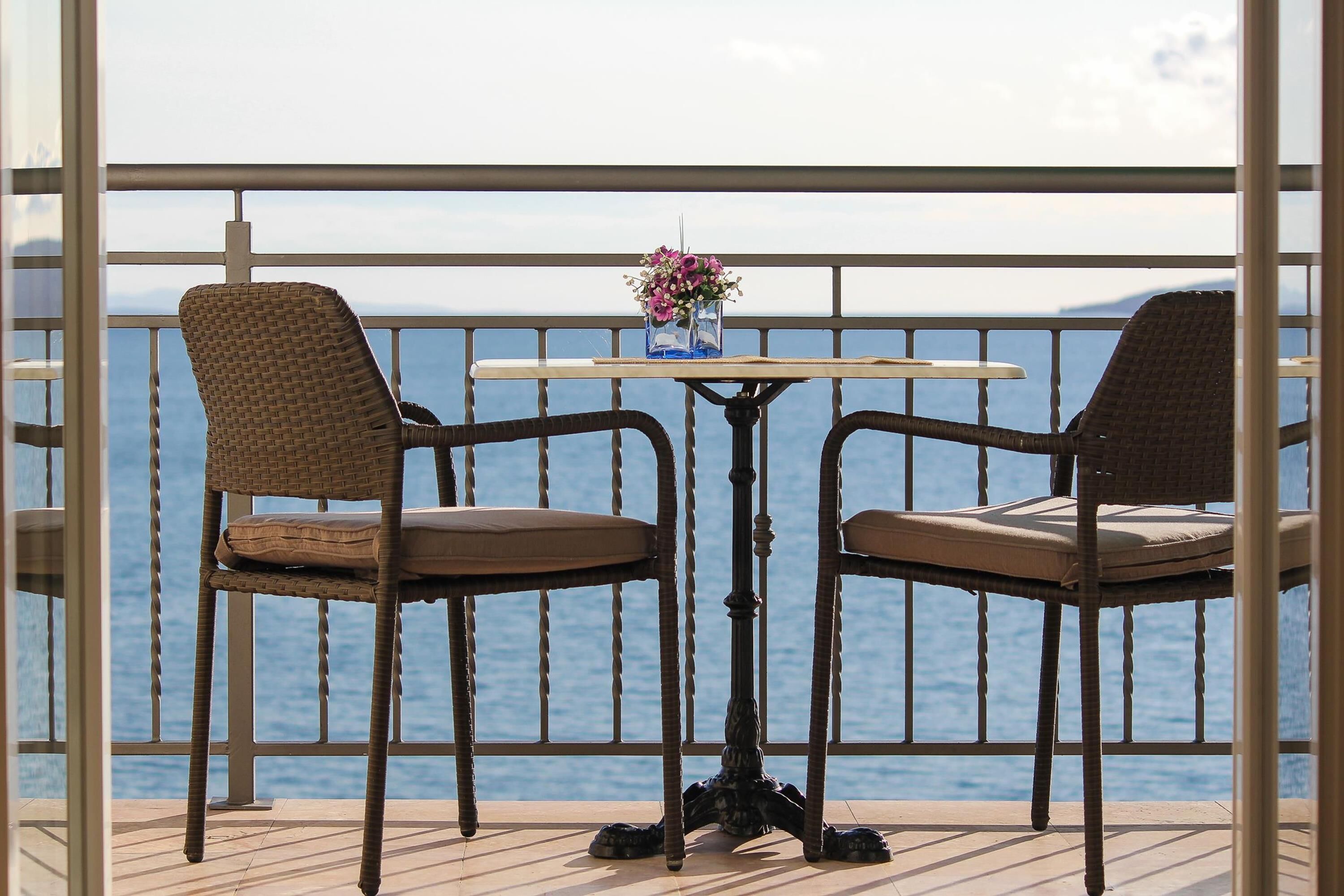 A balcony with wicker chairs and a table, overlooking a body of water.