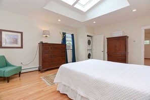 Quarto com clarabóia, cama, cômoda, máquina de lavar e uma cadeira verde.