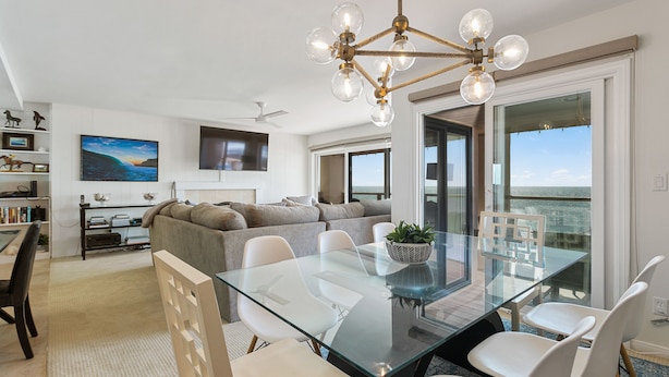 Un salon moderne avec une table à manger en verre, des chaises blanches, un canapé gris et un ventilateur de plafond.