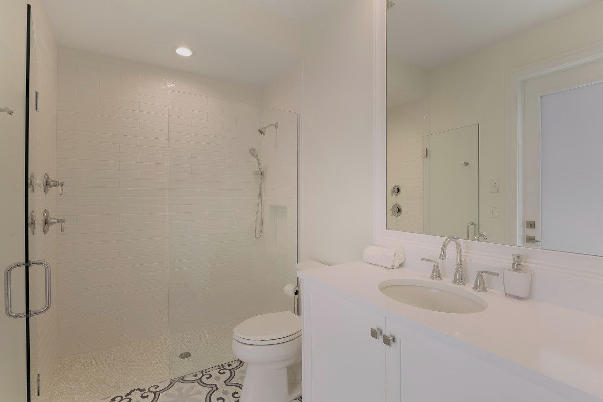 A modern bathroom with a glass-enclosed shower, a white toilet, and a vanity with a sink and mirror.