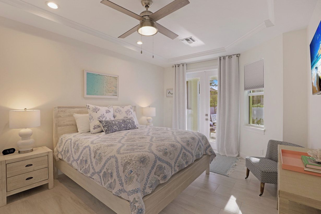 A bedroom with a bed, bedside lamps, a nightstand, a ceiling fan, a window with curtains, and a chair.