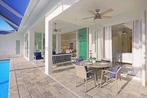 A covered outdoor area with a pool, a dining table with chairs, and a seating area with a sofa and chairs. - Beachy Home | Pool and Steps to Beach/Food/Shops (Marco Island)