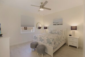 A bedroom with a bed, bedside lamps, a ceiling fan, a window with blinds, and a nightstand with a lamp. - Beachy Home | Pool and Steps to Beach/Food/Shops (Marco Island)