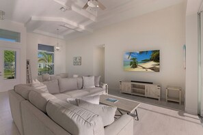 A modern living room with a large sectional sofa, a coffee table, and a flat-screen TV mounted on the wall.