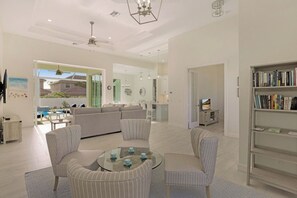 A spacious living room with a glass coffee table, striped armchairs, a bookshelf, and a view of the backyard. - Beachy Home | Pool and Steps to Beach/Food/Shops (Marco Island)