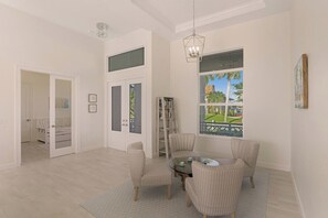 A spacious living room with a round coffee table, striped armchairs, a bookshelf, and a large window with a view of a garden. - Beachy Home | Pool and Steps to Beach/Food/Shops (Marco Island)