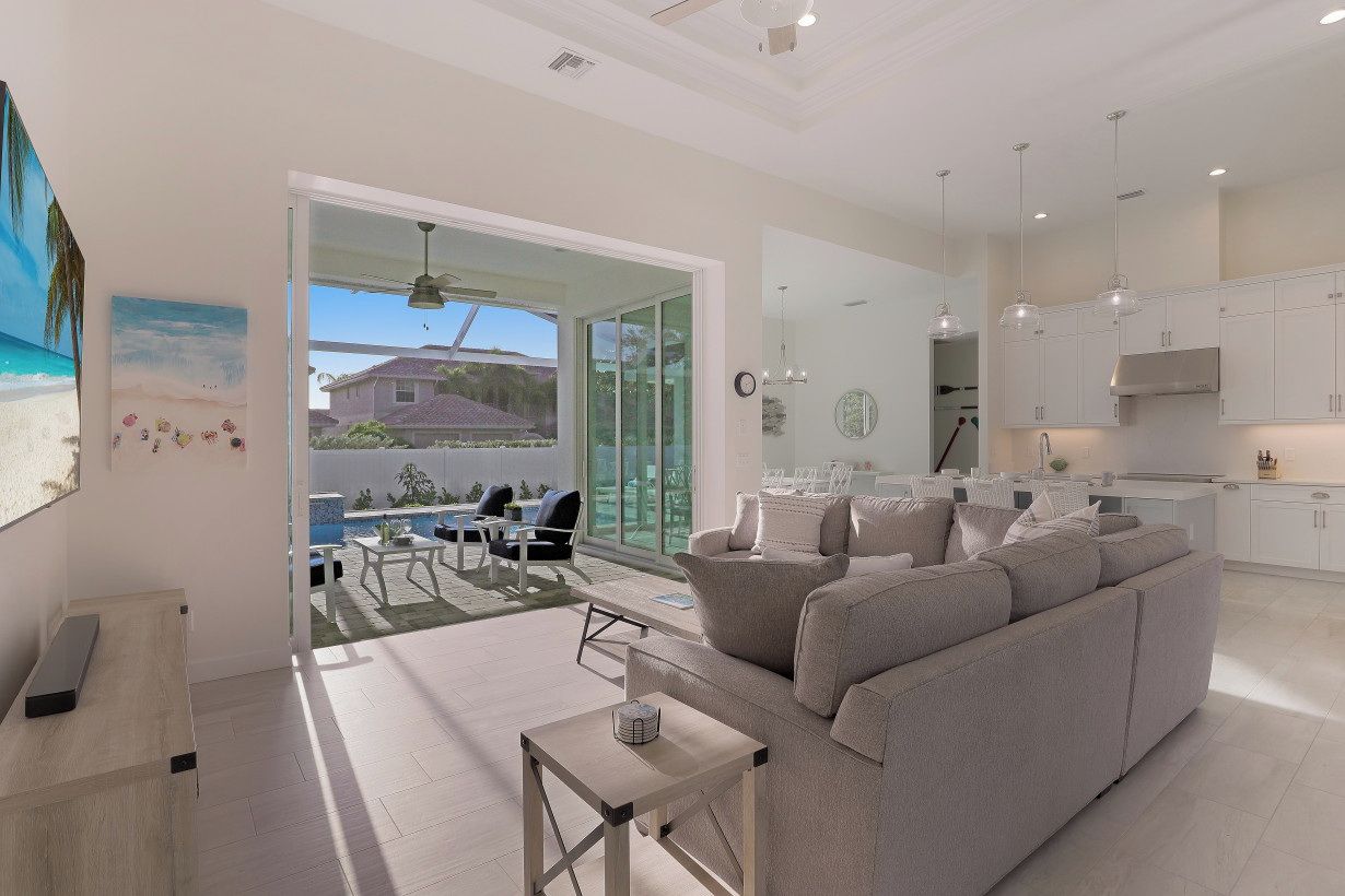 A modern living room with a large sofa, a coffee table, and a dining area with a table and chairs. There is a kitchen area with cabinets and a stove.