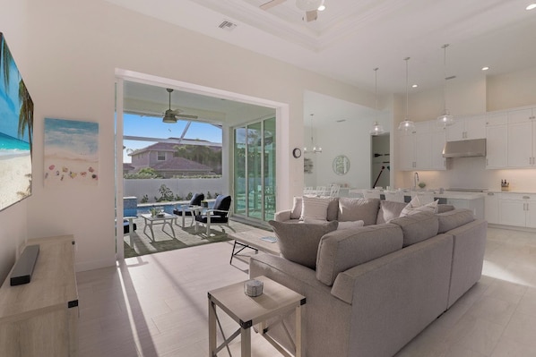 A modern living room with a large sofa, a coffee table, and a dining area with a table and chairs. There is a kitchen area with cabinets and a stove.