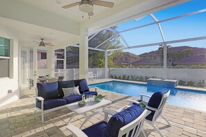 A covered outdoor area with a pool, a sofa, and chairs. - Beachy Home | Pool and Steps to Beach/Food/Shops (Marco Island)