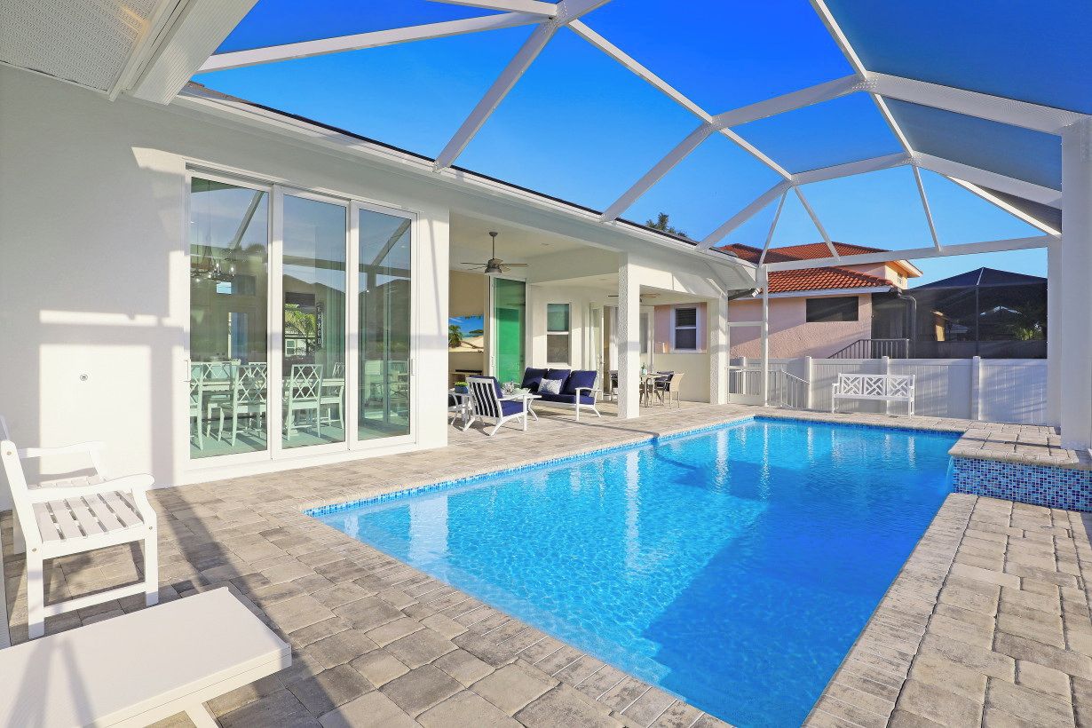 A swimming pool with a glass enclosure, white furniture, and a clear blue sky.