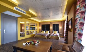 A hotel room with a wooden dining table, two beds with floral bedding, and a large mirror. - Bayberd Hotel (Bayburt)