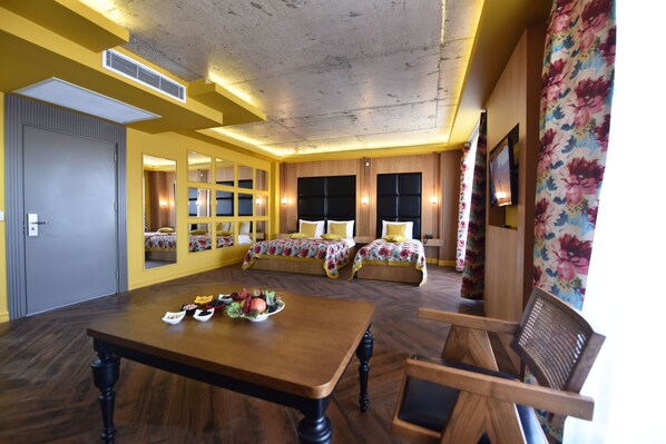 A hotel room with a wooden dining table, two beds with floral bedding, and a large mirror.