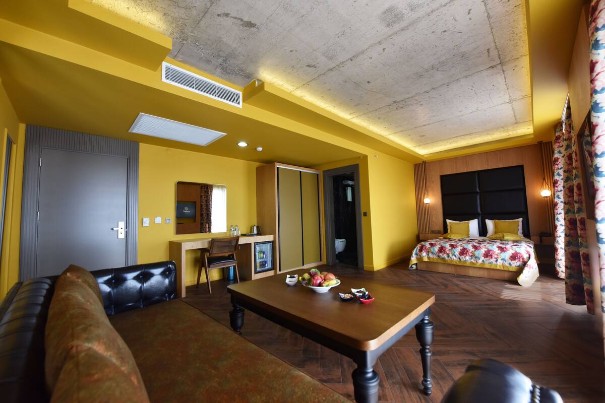 Habitación de hotel con cama, sofá, mesa de comedor con fruta, escritorio y baño.
