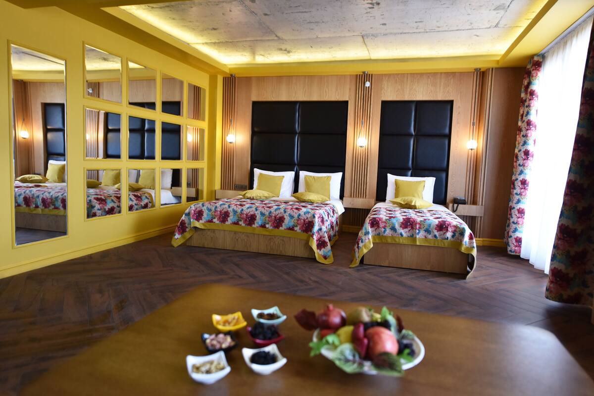 Habitación de hotel con dos camas, paneles de madera y una mesa de desayuno con frutas y pasteles.