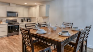 Une cuisine moderne avec des meubles blancs, une table à manger en bois pour six personnes et un four encastré.