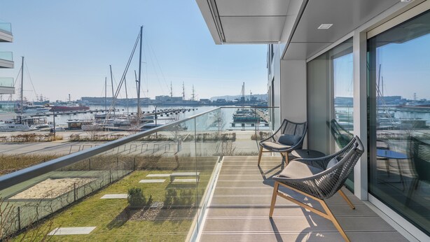 A balcony with a view of a marina, featuring two wicker chairs and a glass railing. - Yacht Park Apartamenty Sun & Snow Nabrzeże (Gdynia)