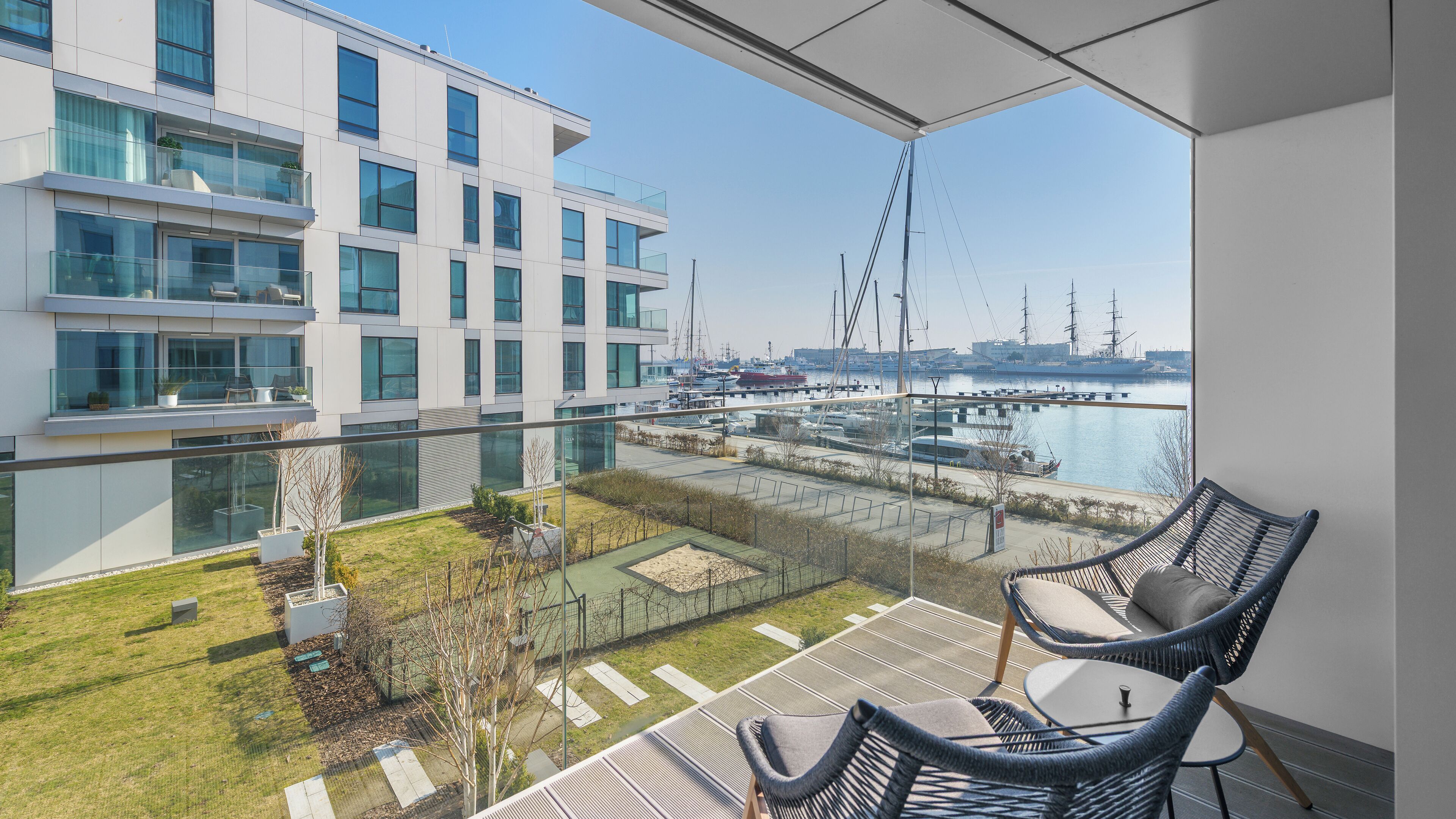 Un balcón con vistas a un puerto deportivo, un edificio moderno y una zona de estar al aire libre.