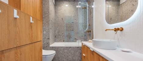 Un baño moderno con tocador de madera, un lavamanos blanco, cabina de ducha con mampara de vidrio y un inodoro.