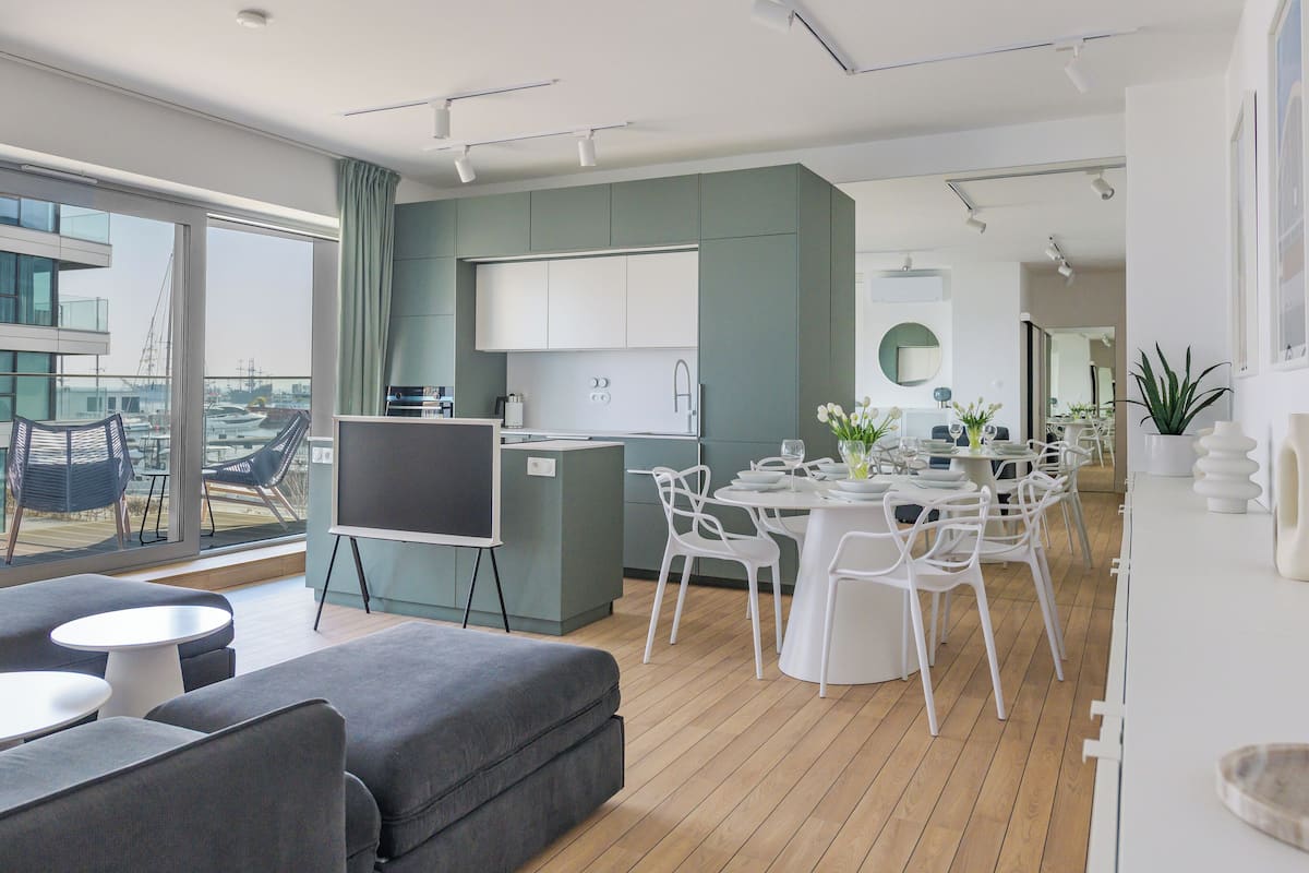 Un salon moderne avec un canapé, un téléviseur et un coin repas comprenant des chaises blanches et une table.