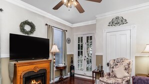 A living room with a fireplace, a television, a ceiling fan, and a door with glass panels. - Private 3 room Queen Suite w/Kitchenette  (Port Deposit)
