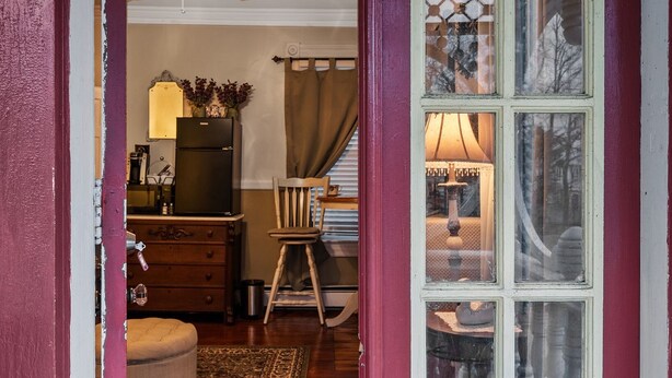 A room with a wooden floor, a ceiling fan, a refrigerator, a chair, a lamp, and a window with curtains. - Private 3 room Queen Suite w/Kitchenette  (Port Deposit)