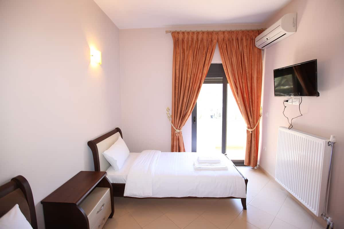 A bedroom with a bed, a wooden nightstand, a TV mounted on the wall, and an air conditioning unit.