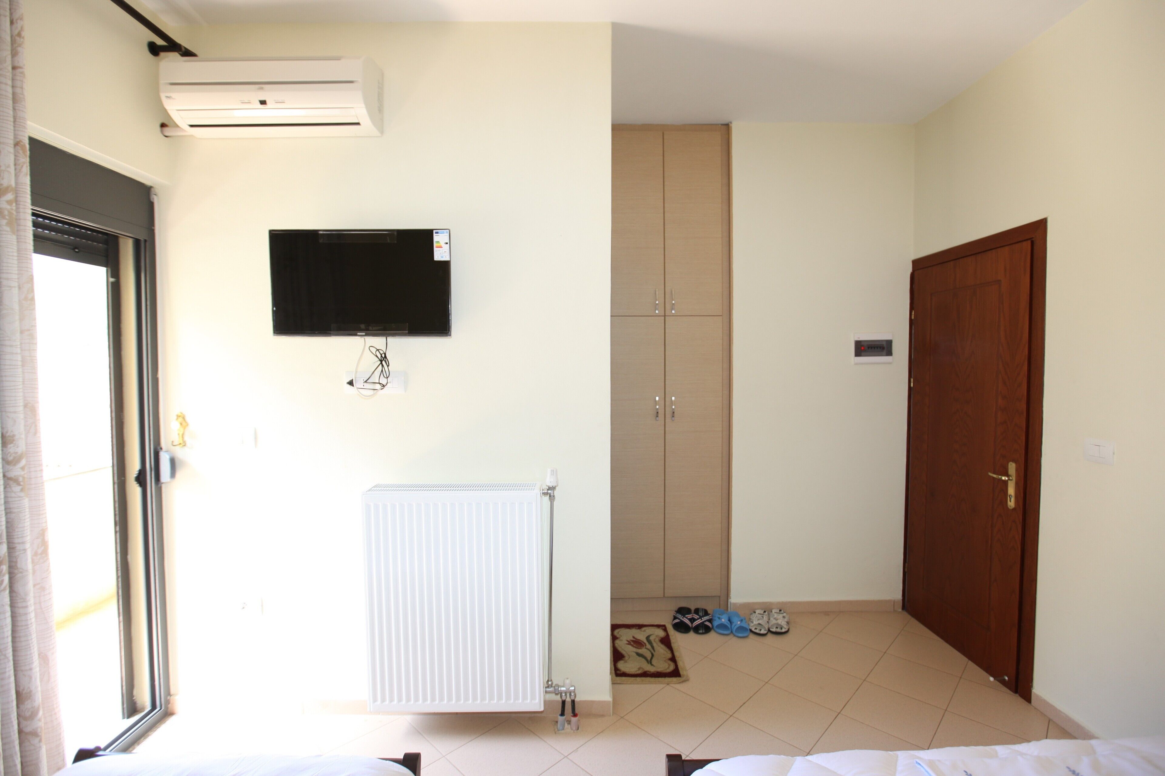 A room with a bed, a radiator, a television mounted on the wall, a wardrobe, and a door.