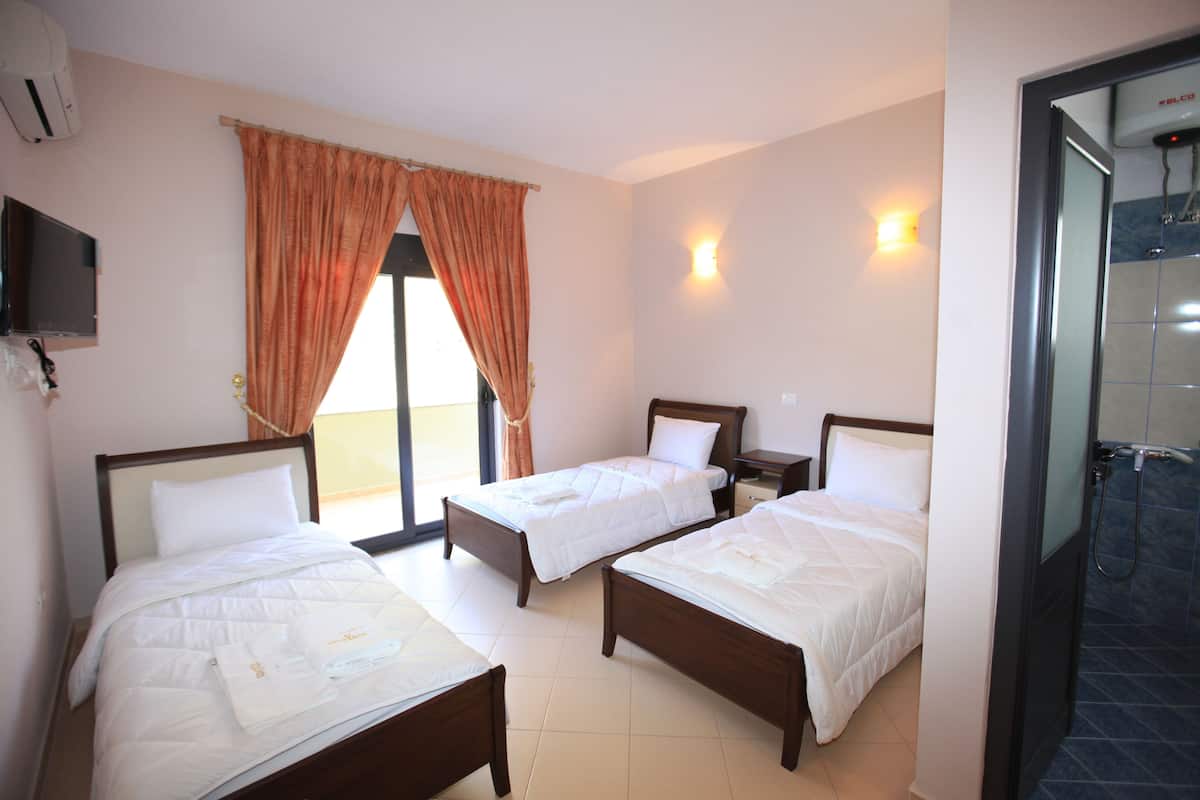 A hotel room with three beds, a television, a window with curtains, and a shower area.