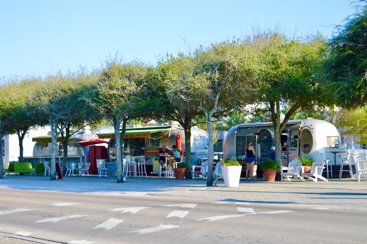 Una calle con terrazas, un carrito de comida y un servicio de alimentos móvil.