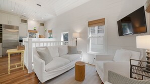 Un vaste espace de vie comprenant un canapé blanc, une table basse en bois et un téléviseur fixé au mur.
