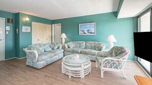 A living room with teal walls, a floral sofa, a round coffee table, and a wicker chair. - 2 Bedroom Condo With Ocean View and Outdoor Pool! (Ocean City)