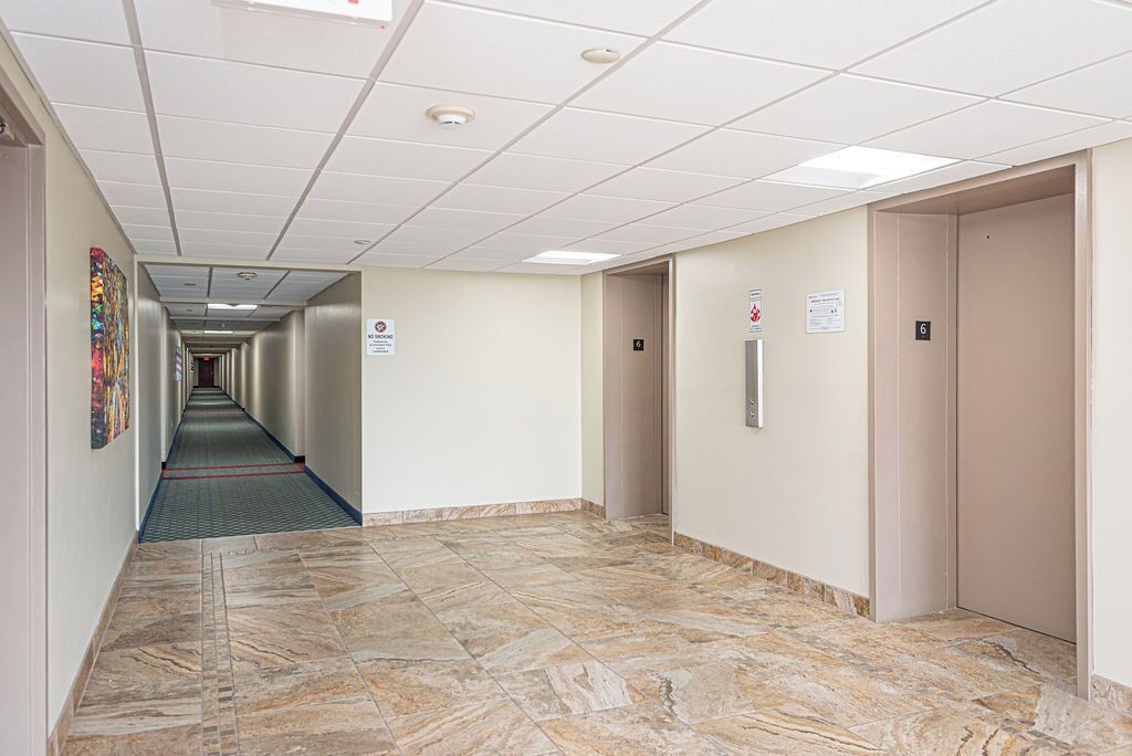 A hallway with a tiled floor, a fire alarm, and an elevator.
