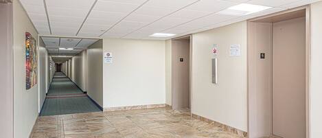 A hallway with a tiled floor, a fire alarm, and an elevator.