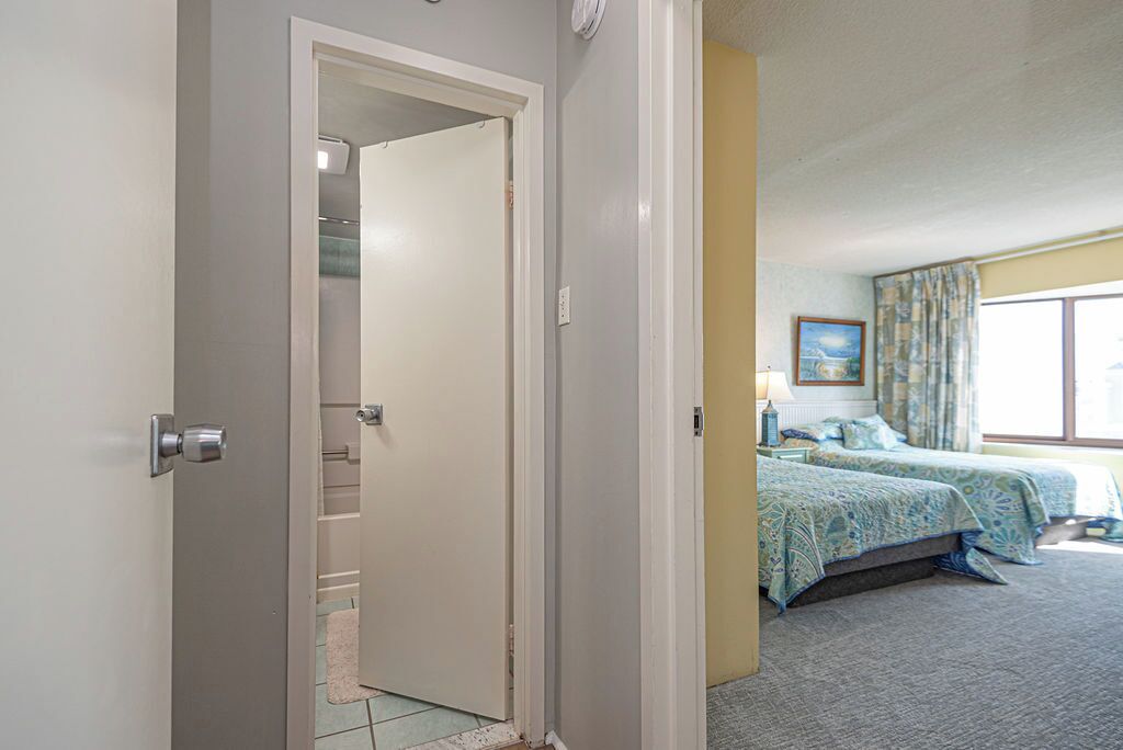 Une chambre d’hôtel comprenant un lit, une table de chevet, une lampe, une fenêtre avec des rideaux et une porte donnant sur un placard.