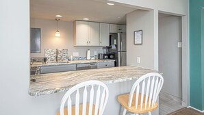 A kitchen with white cabinets, a marble countertop, and two white chairs. - 2 Bedroom Condo With Ocean View and Outdoor Pool! (Ocean City)