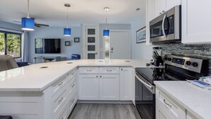 A modern kitchen with white cabinetry, a large island, a built-in microwave, and a stove. - 44 Forest Gardens: Luxurious Remodeled Villa, Walk to Beach, Pool, Free Bikes (Hilton Head Island)