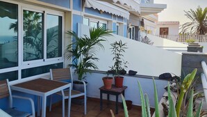 Ein Balkon mit Tisch und Stühlen, Blumentöpfen und Blick aufs Meer.