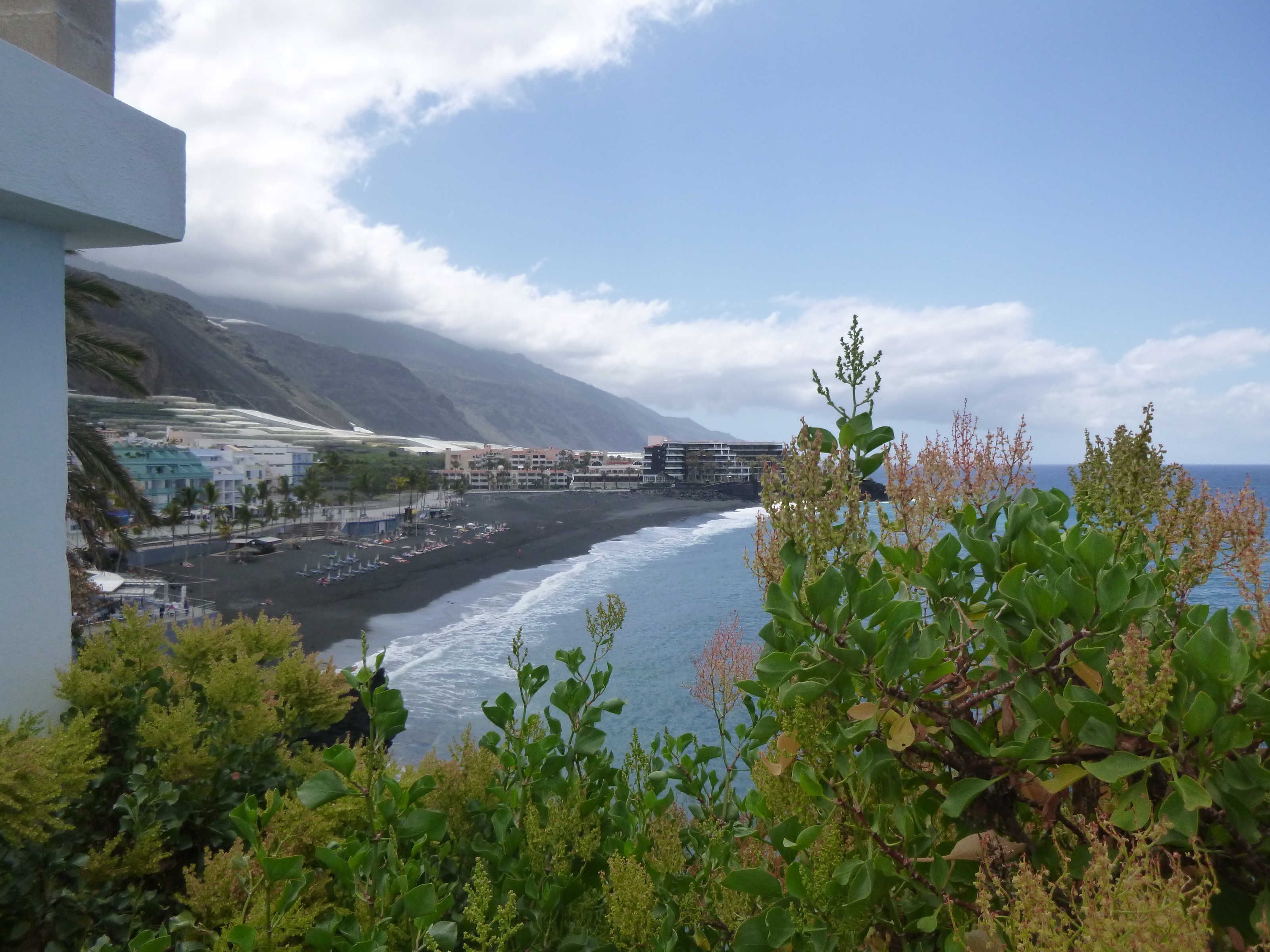 Une vue côtière avec une plage, des bâtiments et des montagnes en arrière-plan.