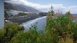 Blick auf die Küste mit Strand, Gebäuden und Bergen im Hintergrund.