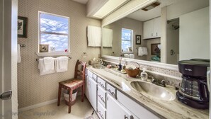 A bathroom with a large mirror, a sink, a chair, and a window with a view of the sky. - Binky's Nest 1 Bedroom Home by RedAwning (Fredericksburg)