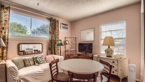 A cozy living room with a white sofa, a round table, and chairs. There is a television, a lamp, and a radiator. - Binky's Nest 1 Bedroom Home by RedAwning (Fredericksburg)