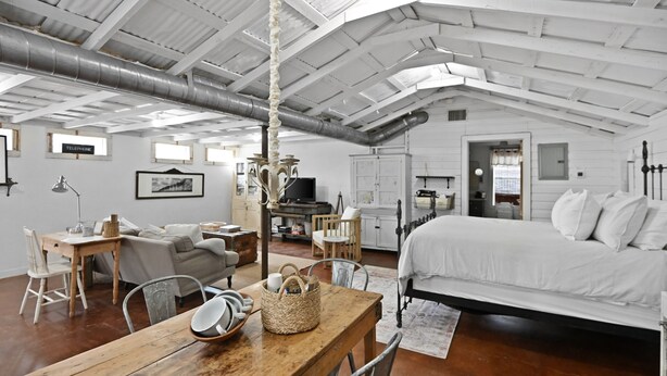 A spacious room with a large bed, wooden table, and chairs. There is a television and a cabinet in the background.