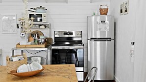 A compact kitchen with a microwave, oven, and refrigerator. There is a wooden table with a bowl of dishes and a basket.