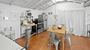 A compact kitchen with modern appliances, a dining table with metal chairs, and a white ceiling with exposed beams.